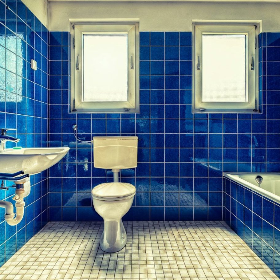 Badezimmer mit blauen Fliesen, WC, Waschbecken und Badewanne an der Wand.