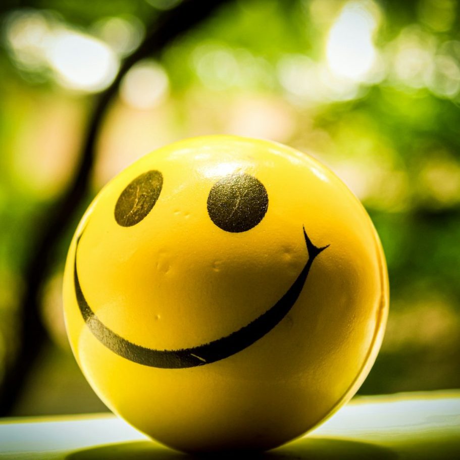 Gelbe Ball mit Smiley-Gesicht und lächelnden Augen vor unscharfem Hintergrund.