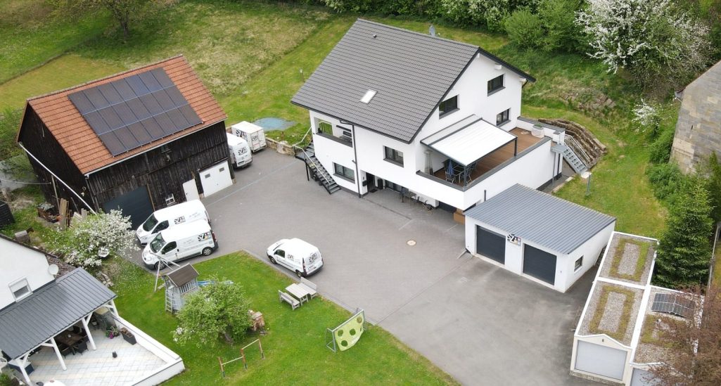 Gebäude SZ Sanitär-Heizung Schneebedeckte Landschaft mit einem Haus und Garagen, umgeben von Bäumen.